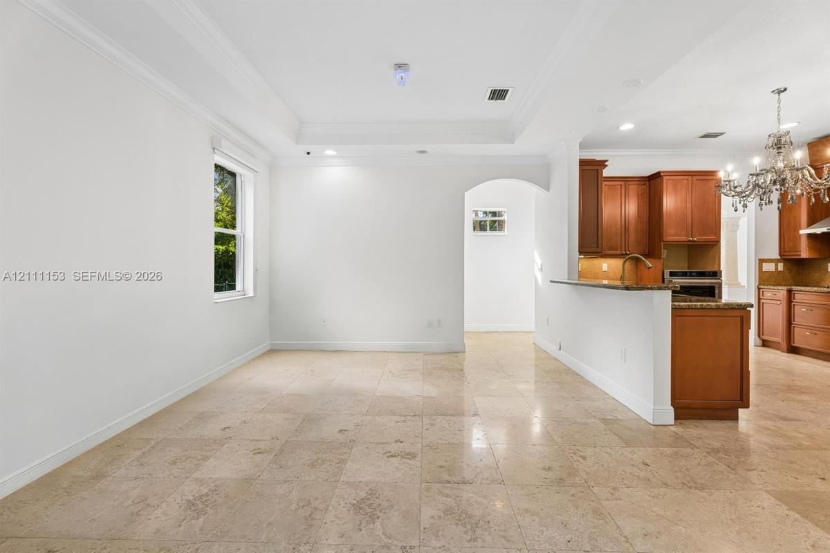 Tray ceiling with crown molding, stone tile flooring, arched entryway, wooden cabinetry, and peninsula-style countertop