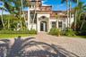 Mediterranean-inspired exterior featuring a clay tile roof, arched entryway with classical columns, stucco facade, multi-story glass window panel, and