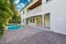 Stucco exterior featuring a second-story balcony with balustrades, a covered patio with columns, wood-paneled ceiling, and a paver pool deck
