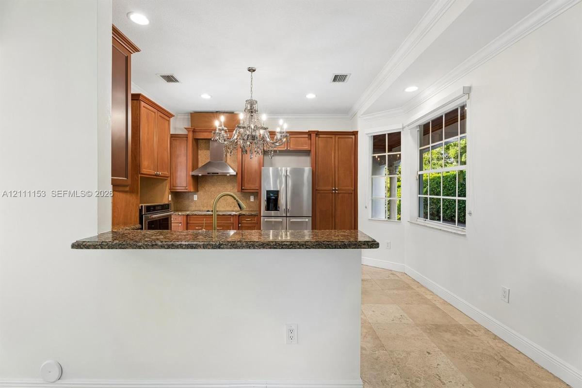 Kitchen featuring raised-panel wood cabinetry, stone countertops, stainless steel appliances, a decorative crystal chandelier, and natural stone floor