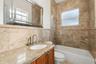 Stone-surround bathtub, vanity with stone countertop, undermount sink, brushed nickel faucet, and wood-finish cabinetry