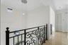Hallway featuring polished stone flooring, intricate black iron railing, multi-tiered pendant lighting, crown molding, and louvered closet doors