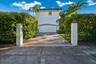 Stucco exterior featuring a paver driveway, arched garage entry, decorative stucco pillars, and mature landscaping