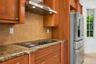 Kitchen featuring wood cabinetry, stone countertops, a glass cooktop, a stainless steel chimney-style range hood, and a stainless steel French door re