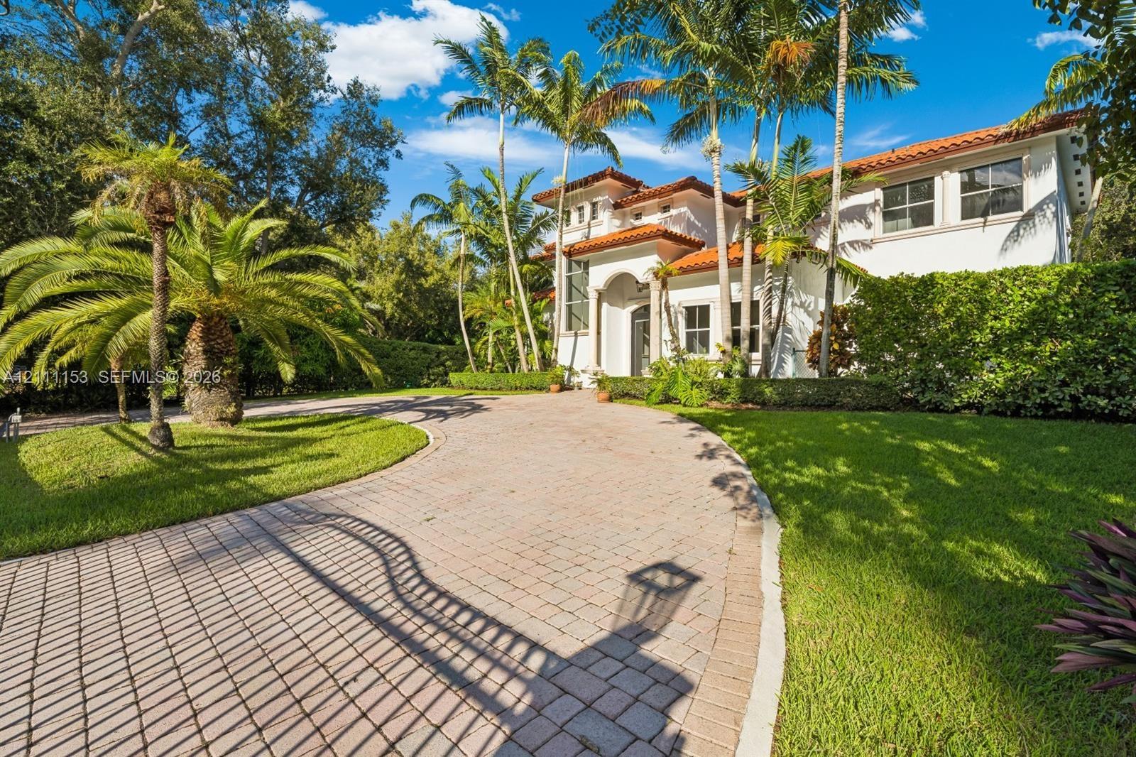 Stucco exterior featuring a terracotta tile roof, arched entryway, paved driveway, and mature palm landscaping