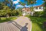 Stucco exterior featuring a terracotta tile roof, arched entryway, paved driveway, and mature palm landscaping