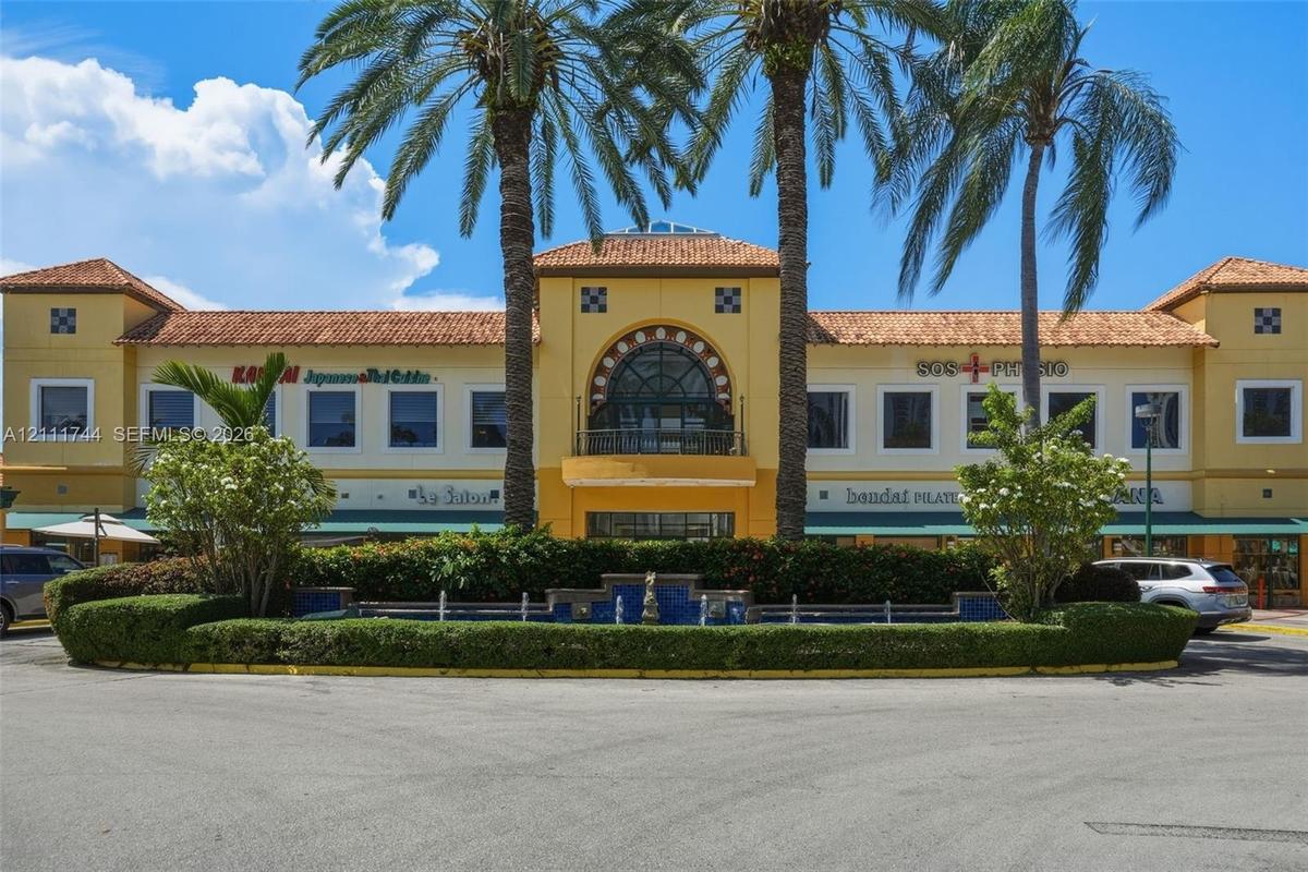 Mediterranean-inspired commercial exterior featuring a tile roof, decorative arched stonework above the central balcony, a blue-tiled water feature, a