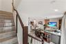 Staircase featuring wood-finish treads, a dark-toned handrail, and white vertical balusters, opening into a living area with large-format tile floorin