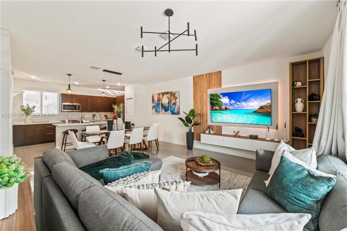 Open-concept living space featuring wood-finish cabinetry, a floating media console with backlighting, vertical wood slat wall accents, and a modern m