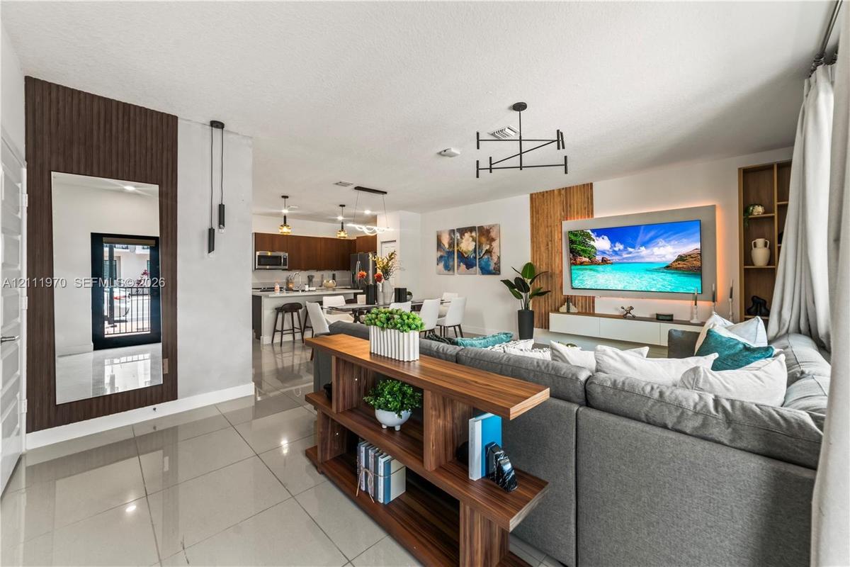 Open-concept interior featuring large-format tile flooring, vertical wood-slat wall accents, contemporary multi-arm light fixtures, a built-in media c