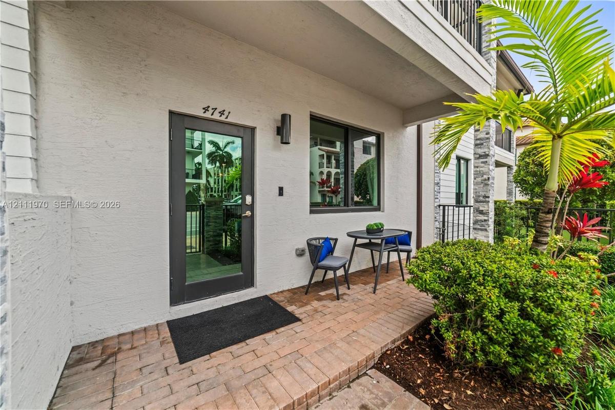 Stucco exterior entryway featuring a brick paver patio, full-light glass door, and a wall-mounted cylinder sconce