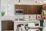 Kitchen featuring dark-stained flat-panel cabinetry, stone countertops, a central island with an integrated sink, stainless steel microwave, and glass