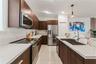 Kitchen featuring flat-panel wood-finish cabinetry, white countertops, stainless steel appliances, a central island with an undermount sink, and tile 