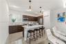 Kitchen featuring dark wood-finish cabinetry, a white stone-surface island, stainless steel appliances, large-format tile flooring, and dual pendant l