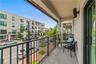 Covered balcony featuring concrete flooring, black metal railing, stone-clad pillar, and mounted exterior lighting