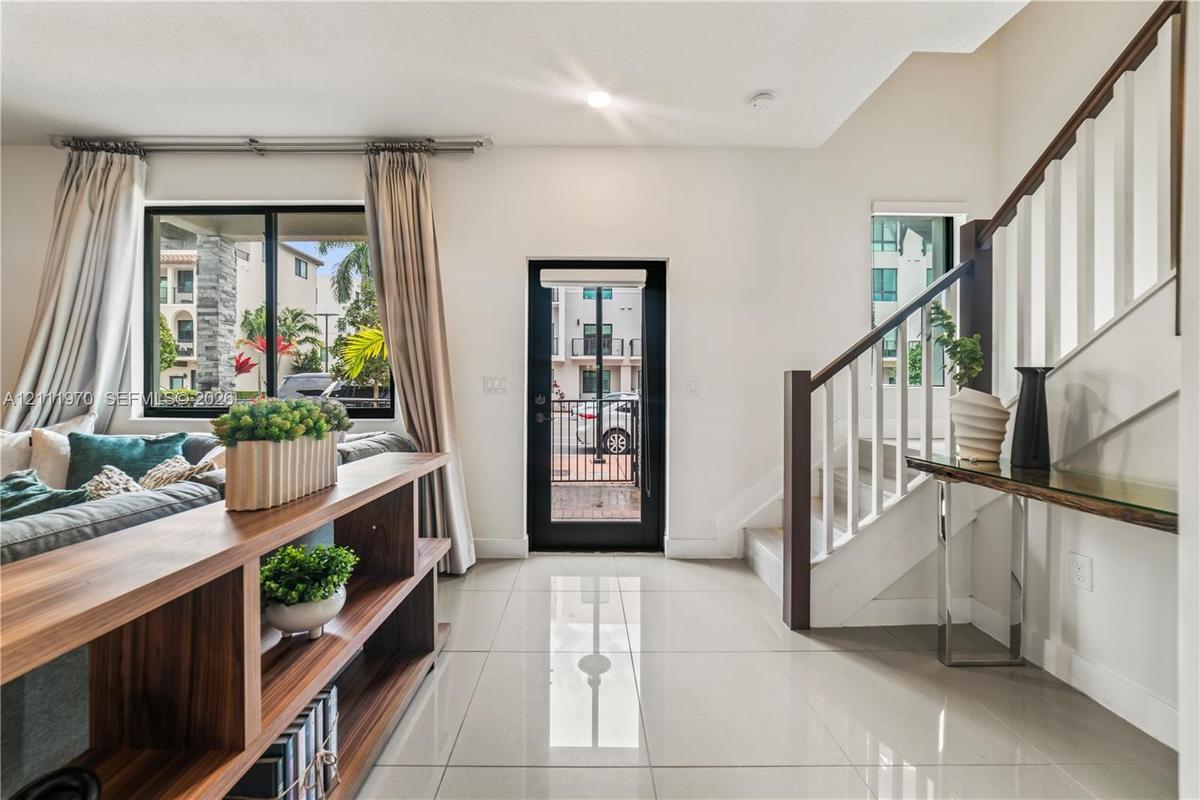Polished large-format tile flooring, black-framed exterior glass door, and staircase featuring white balusters with dark wood handrails