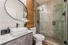 Bathroom featuring a wall-mounted vessel sink, matte black fixtures, textured wave-patterned tile wall, wood-finish paneling, and a glass-enclosed wal