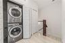 Stacked stainless steel laundry appliances, white paneled bi-fold closet doors, tile flooring, and a wooden handrail with vertical balusters