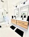 Dual floating wood-finish vanities with rectangular integrated sinks, matte black hardware, geometric mirrors, and a glass-enclosed walk-in shower