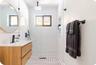 Bathroom featuring a floating wood-finish vanity, circular mirror, walk-in shower with matte black rainfall showerhead, and a built-in wall niche