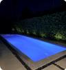 Rectangular pool with submerged stairs, bordered by large-format concrete pavers, decorative stone aggregate, and a manicured hedge