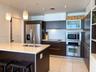 Kitchen featuring dark-finish cabinetry, stone-surface countertops, stainless steel appliances, a central island with a double-basin sink, and recesse