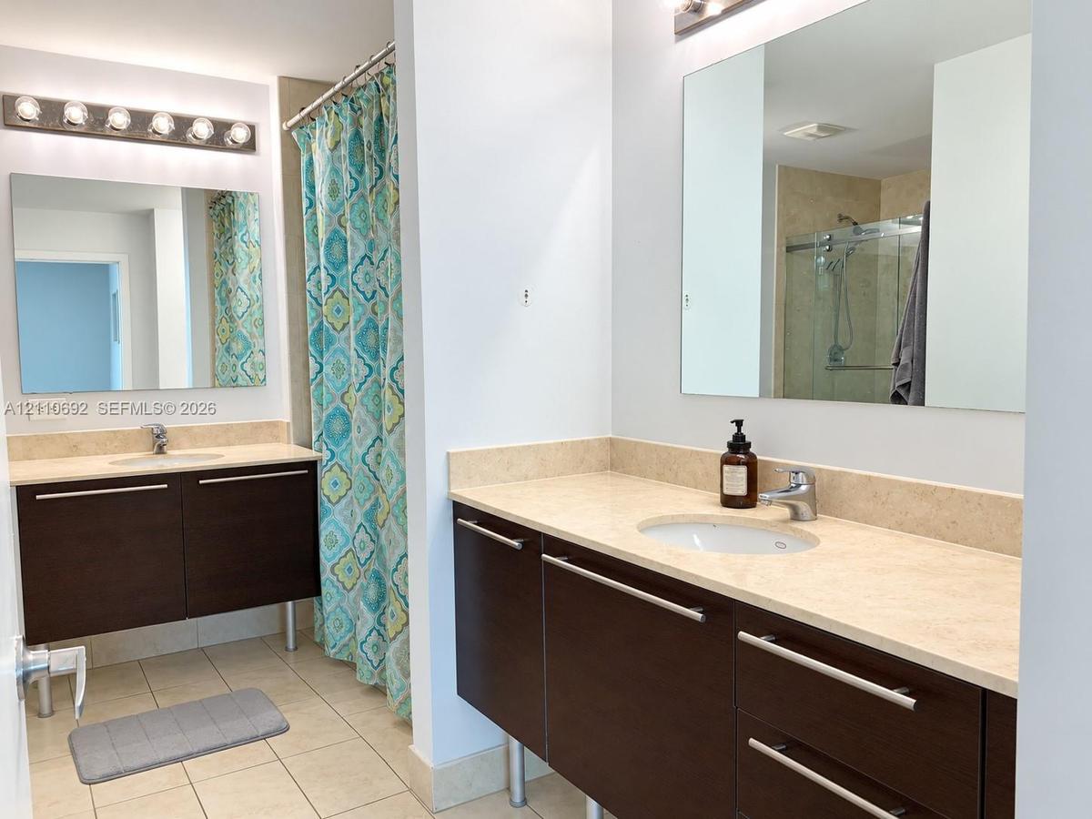 Dual floating vanities featuring dark wood-finish cabinetry, light-toned stone countertops, undermount sinks, and polished hardware, complemented by f