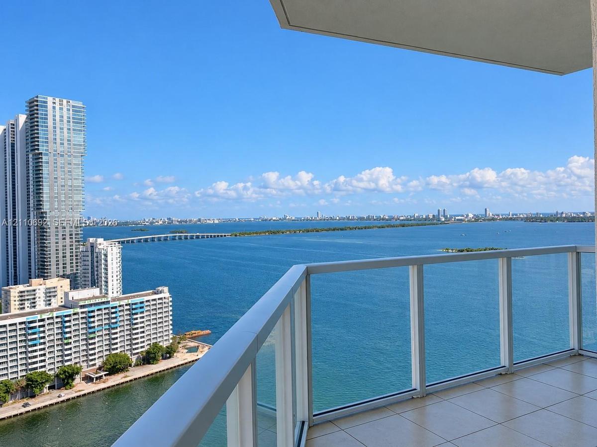 Private balcony featuring glass panel railings and tile flooring, offering expansive water and cityscape scenery