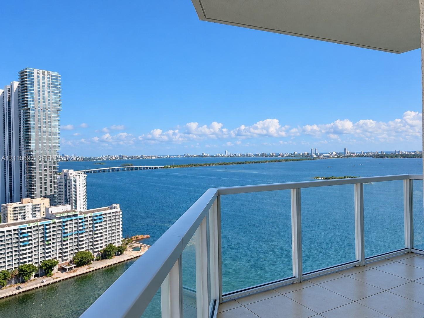 Private balcony featuring glass panel railings and tile flooring, offering expansive water and cityscape scenery