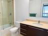 Bathroom featuring a dark wood-finish vanity with a light-toned countertop, integrated oval sink, glass-enclosed shower-tub combination with tile surr