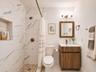 Bathroom featuring a walk-in shower with stone-look wall tile, a pebbled floor, and an integrated wall niche, complemented by a wood-finish vanity and