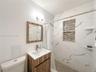 Bathroom featuring a vanity with a white countertop, wall-mounted light fixture, mirror with a wood-finish frame, and a shower area with large-format 