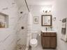 Bathroom featuring a walk-in shower with stone-patterned wall tile, a recessed storage niche, a pebble-finish floor, a wood-finish vanity with a recta