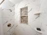 Shower surround finished with large-format white veined tile, a multi-tier built-in tiled niche with decorative mosaic detailing, two integrated corne
