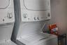 Stacked white laundry appliance unit featuring a top-load washer and front-control drying interface