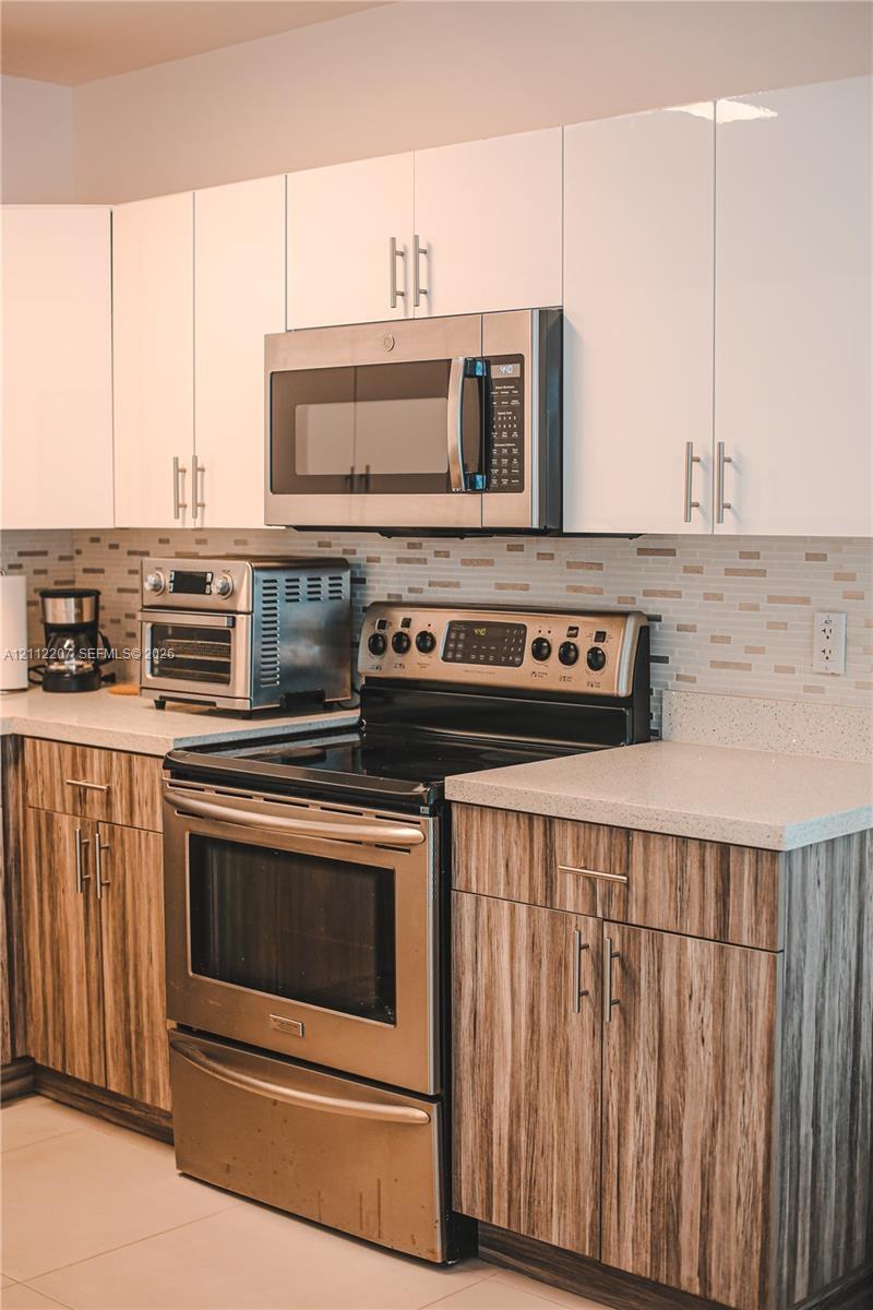 Kitchen featuring high-gloss white upper cabinetry, wood-finish lower cabinetry, stone-composite countertops, stainless steel appliances, and a linear