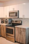 Kitchen featuring high-gloss white upper cabinetry, wood-finish lower cabinetry, stone-composite countertops, stainless steel appliances, and a linear