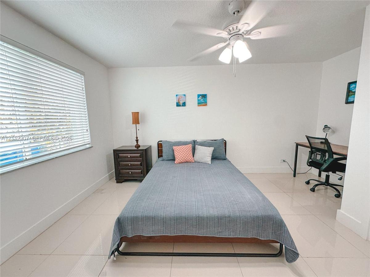 Neutral wall finishes, large-format tile flooring, white horizontal window blinds, and a white ceiling fan with integrated lighting