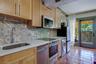 Kitchen featuring light wood cabinetry, patterned tile backsplash, solid surface countertops, stainless steel appliances, and terracotta tile flooring