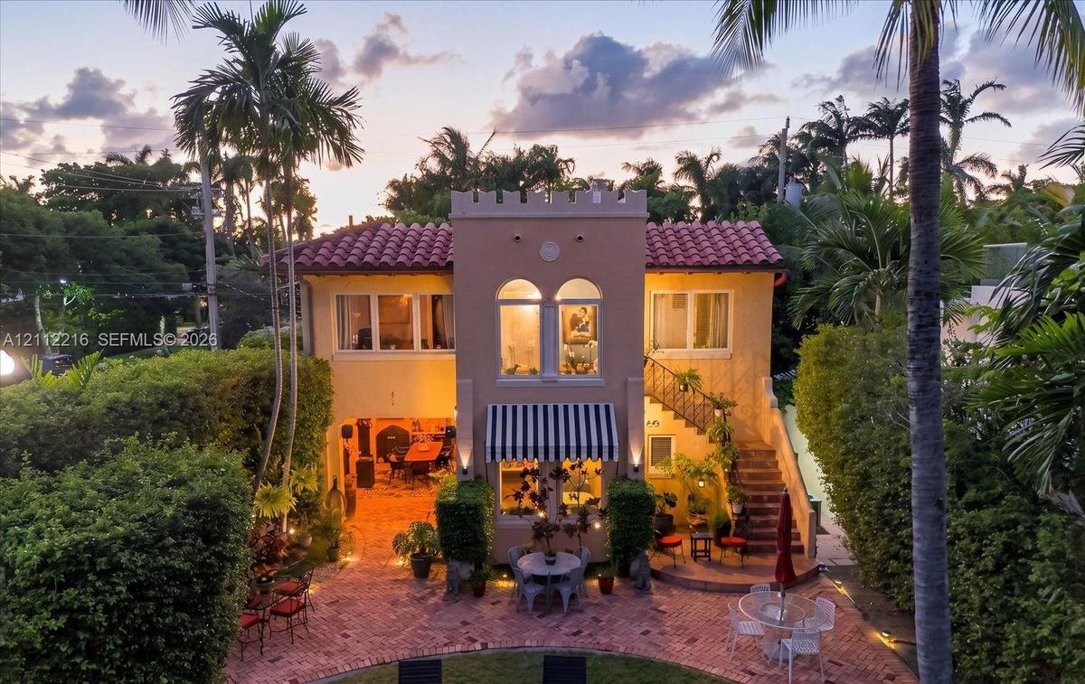 Mediterranean-style exterior featuring a terracotta tile roof, crenellated parapet, arched second-story windows, external staircase, and paved brick p