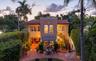 Mediterranean-style exterior featuring a terracotta tile roof, crenellated parapet, arched second-story windows, external staircase, and paved brick p