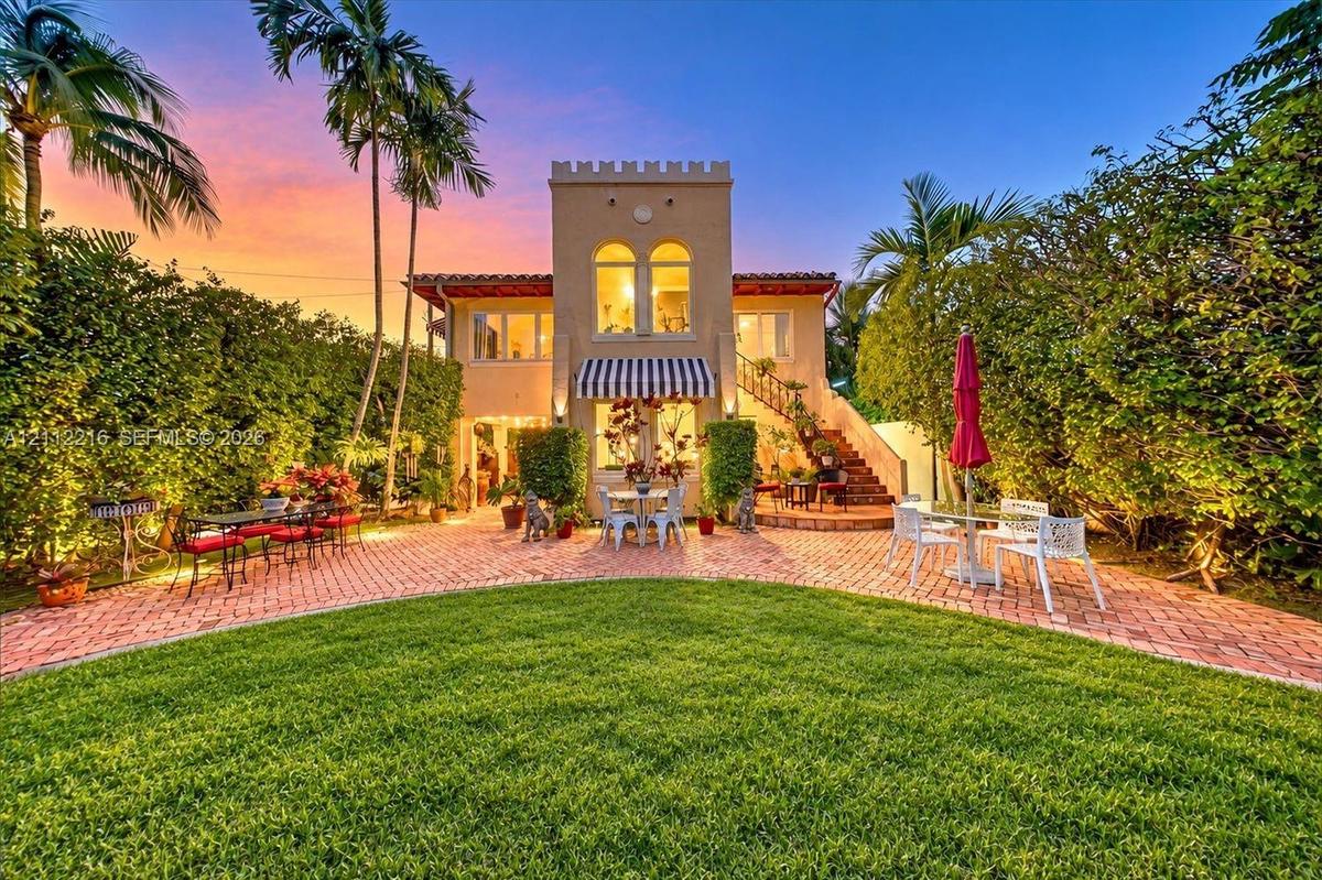 Mediterranean-inspired exterior featuring a crenelated roofline, brick paver patio, arched window detailing, exterior masonry staircase, and a manicur