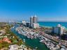 Aerial perspective of coastal landscape featuring a deep-water marina, ocean coastline, expansive high-rise structures, and residential properties wit