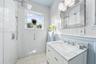Bathroom featuring a white vanity with a stone countertop, a glass-enclosed shower with pebble-stone flooring, subway tile wall cladding, and a framed