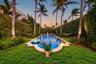 Rectangular swimming pool featuring a decorative stone coping, manicured lawn, perimeter hedge landscaping, and mature palm trees