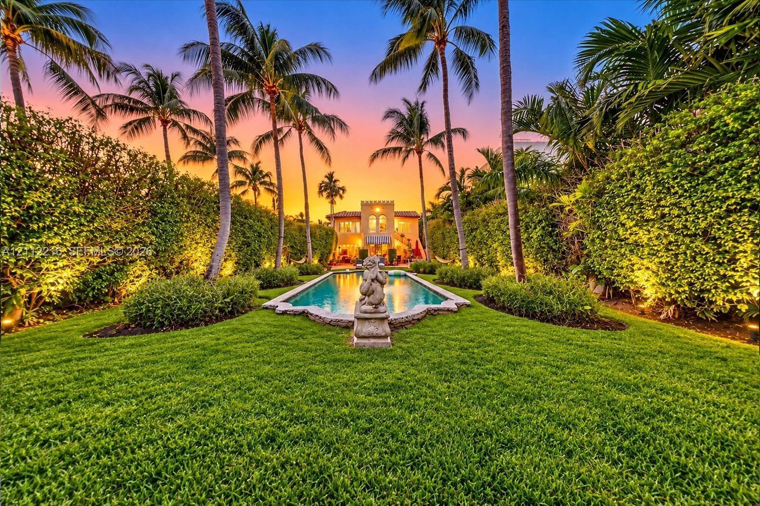 Expansive backyard featuring a rectangular swimming pool, stone sculpture, manicured lawn, and mature palm trees framed by high-density hedges