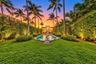 Expansive backyard featuring a rectangular swimming pool, stone sculpture, manicured lawn, and mature palm trees framed by high-density hedges