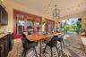 Covered patio featuring stone paver flooring, outdoor kitchen cabinetry, red-framed glass double doors, an overhead iron chandelier, and string lighti