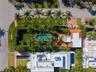 Aerial perspective of a multi-structure property featuring a swimming pool, a second elongated swimming pool, expansive manicured lawn, and mature per
