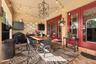 Covered patio featuring brick flooring, dual glass-paned doors with bold red frames, decorative glass block accents, and an overhead geometric chandel
